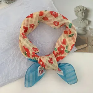 Vista detallada de un pañuelo de seda con flores rojas y extremos de rayas azules