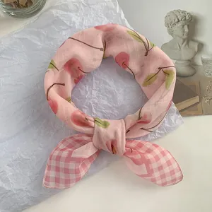 Primer plano de bufanda de seda rosa con estampado de cerezas y detalle vichy