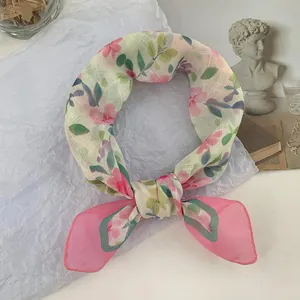 Primer plano de un pañuelo de seda con flores rosas anudado como una bufanda corta.