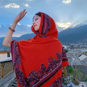 Asian model wearing a large red ethnic print shawl on a scenic rooftop during sunset.