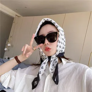 Model styling a white satin silk-like headscarf with black letter D monogram pattern