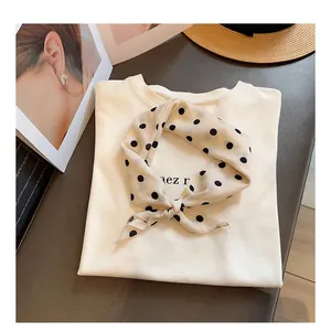 Detalle de un pañuelo de seda de lunares de estilo chic francés anudado en una camiseta crema