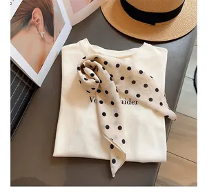 Elegante detalle de pañuelo de seda con lunares estilo francés sobre top crema