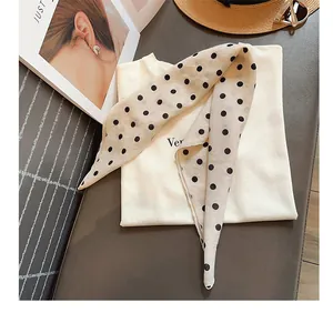 Primer plano de un pañuelo color crema con lunares negros sobre una camiseta blanca lisa