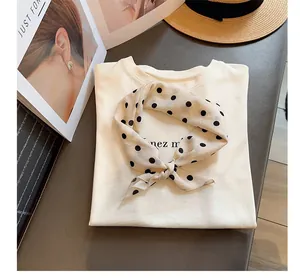 Primer plano de elegante pañuelo de seda beige con lunares anudado en camiseta