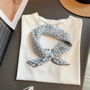 Pañuelo cuadrado con flores azules anudado sobre una camiseta blanca