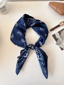 Detailed shot of a navy blue paisley silk scarf knotted on a minimalist background.
