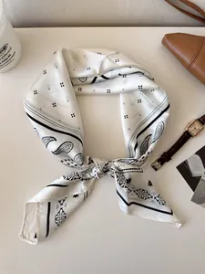 Detailed view of white paisley silk scarf tied in a stylish knot on a tabletop