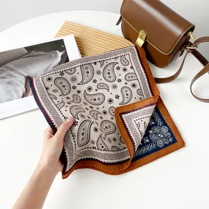 Close-up of a vintage paisley square scarf held by hand next to a brown leather bag