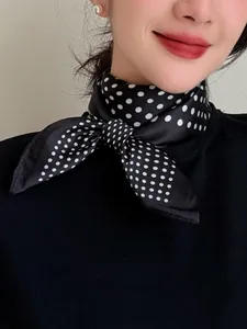 Elegant close-up of a black silk neck scarf featuring classic white polka dots on model