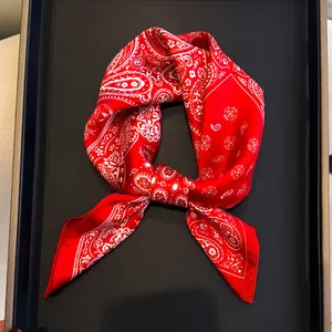 Elegant red silk square scarf with white paisley pattern on black display tray