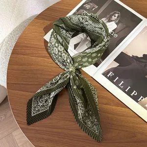 Close-up detail view of a pleated olive green paisley scarf with a gold ring on a wooden table
