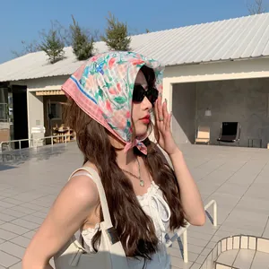 Model wearing a pink floral cotton linen small square headscarf in a sunny outdoor cafe.