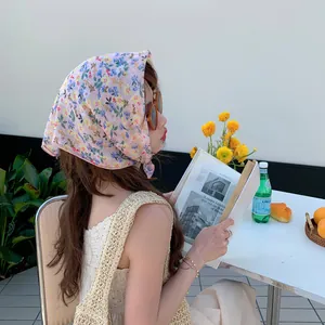 Model wearing a pink floral cotton-linen headscarf in an outdoor cafe setting
