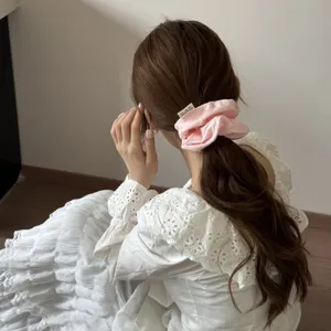 Détail d'un chouchou rose tendre en tissu sur une queue de cheval brune ondulée.
