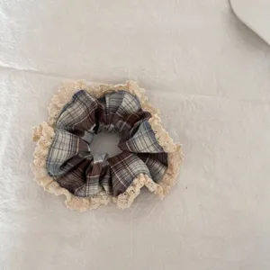Detailopname van een dubbellaagse geruite scrunchie met elegante beige kanten randen