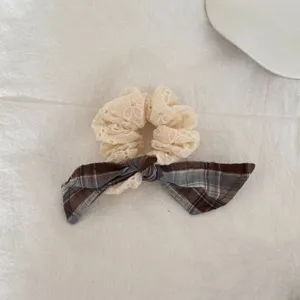 Detailopname van een stijlvolle crème kanten scrunchie met een bruine geruite strik