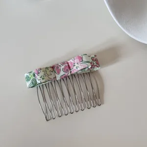 Detailed view of a floral bow hair comb with 10 silver metal teeth on a white surface