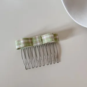 High-angle detailed shot of a green and white plaid bow on a silver metal hair comb