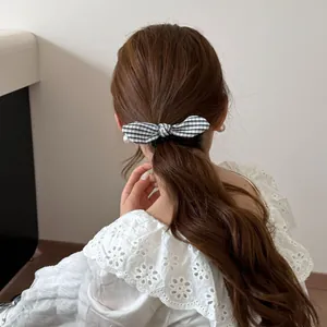 Detalle de un coletero con lazo de cuadros de estilo preppy usado en una coleta baja suave