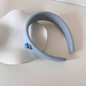 Detailansicht eines gepolsterten blauen Haarreifs mit Punkten und süßen Knopfdetails.