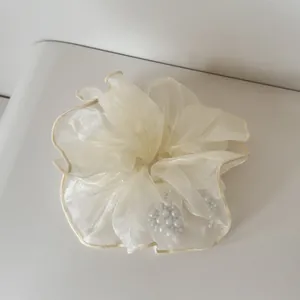 Nahaufnahme eines elfenbeinfarbenen Organza-Scrunchies mit eleganten Kunstperlen-Akzenten.