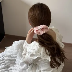 Détail d'un chouchou rose à carreaux sur une queue de cheval brune aux cheveux ondulés