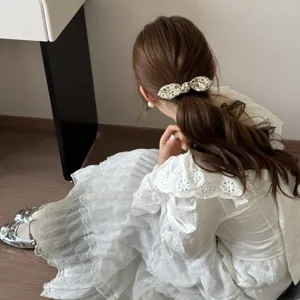 Detail shot of a vintage floral bow hair clip worn on a low ponytail for a soft look