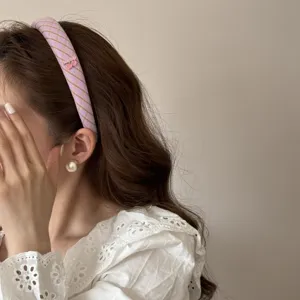 Close-up detail of a purple striped headband with a pink cherry charm on wavy brown hair