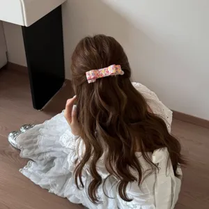 Détail d'une barrette en tissu à fleurs colorées sur de longs cheveux bruns ondulés