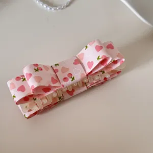 Vue détaillée d'une pince à cheveux en tissu rose avec motifs cœurs et cerises.