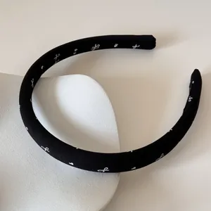 Détail d'un serre-tête en satin noir avec motifs de nœuds blancs sur un support blanc