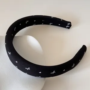 Détail d'un serre-tête en satin rembourré noir avec des motifs de nœuds blancs