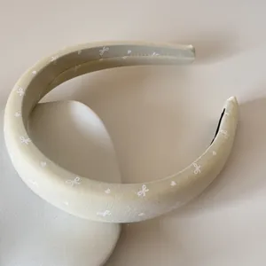 Gros plan d'un serre-tête en satin rembourré beige orné de motifs de nœuds blancs délicats