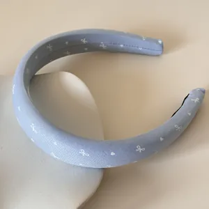 Gros plan d'un serre-tête en satin bleu clair avec de petits motifs cœurs et nœuds blancs