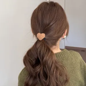 Close-up detail of a brown plush heart hair tie on a low ponytail of wavy brown hair