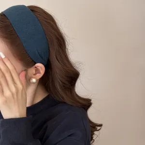Close-up of a wide dark teal ribbed headband and gold stud earrings on a model.
