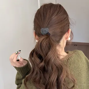 Close-up detail of a plush grey heart-shaped hair tie styling a brunette ponytail.