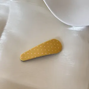 Gros plan d'une barrette à cheveux en tissu jaune à pois sur fond minimaliste