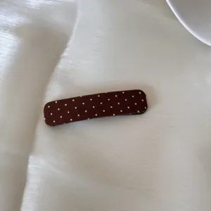 Gros plan d'une barrette à cheveux BB en tissu marron avec un motif à pois blancs élégant.
