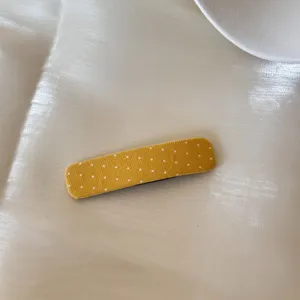 Vue détaillée d'une pince à cheveux en tissu jaune à pois blancs sur fond de soie