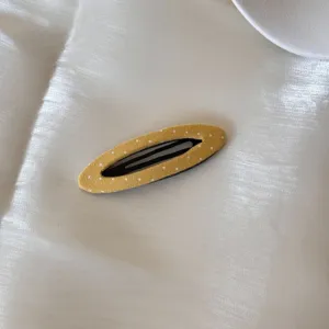 Vue détaillée d'une pince à cheveux jaune à pois en tissu sur fond de soie blanche