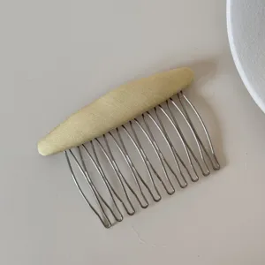 Dettaglio di un pettine per capelli in tessuto giallo con denti in metallo argentato.