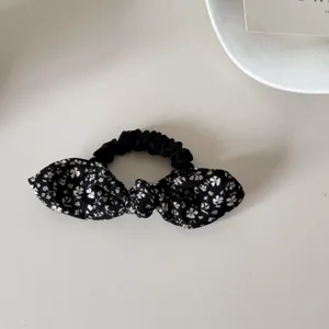 Macro view of a stylish black floral print bow scrunchie on a minimalist white surface