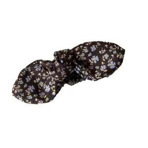 Vintage floral bow hair clip with blue and yellow flowers on a dark fabric background.