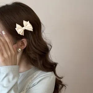 Barrette à cheveux avec nœud en satin crème élégant sur des cheveux bruns ondulés