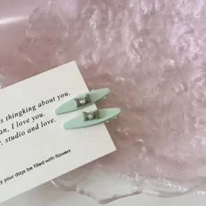 Close-up of mint green duckbill hair clips with rhinestone bow detail on a white card
