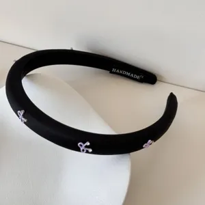 Detalle de diadema acolchada negra con lazos morados y pequeños cristales brillantes.