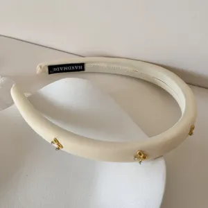 Detalle de diadema de esponja crema con lazo dorado y pedrería etiqueta hecha a mano