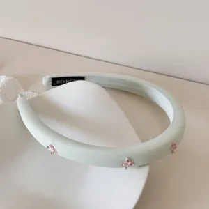 Detalle de una diadema acolchada de color verde menta con lazos rosas y pedrería.